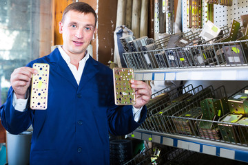 man seller wearing uniform having metal furniture in hands in store