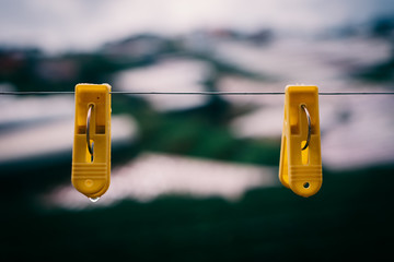 Couple plastic clothes peg. Royalty high quality stock photo of two yellow plastic clothes peg clothespin clipped on outdoor clothesline metal line. Green garden background