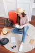 © weedezign - Young asian woman traveler prepare things into orange suitcase for holiday vacation at home.backpacker travel concept.