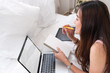 © weedezign - Asian woman laying on bed doing paperwork on laptop in bedroom.work at home.e-larning concept.study online.mock up device.clipping path screen.