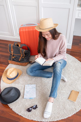 Young asian woman traveler prepare things into orange suitcase for holiday vacation at home.backpacker travel concept.