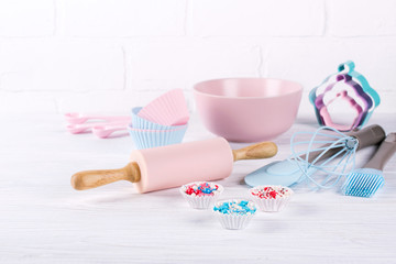 Baking background with kitchen tools: rolling pin, wooden spoons, whisk, sieve, bakeware and shape cookie cutter on white wooden background.