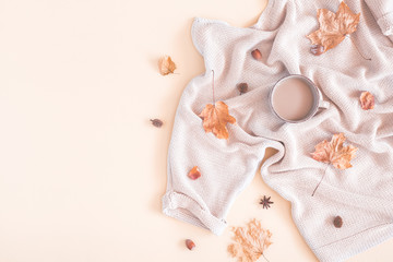 Autumn cozy composition. Cup of coffee, women fashion sweater, dried leaves on pastel beige background. Autumn, fall concept. Flat lay, top view, copy space