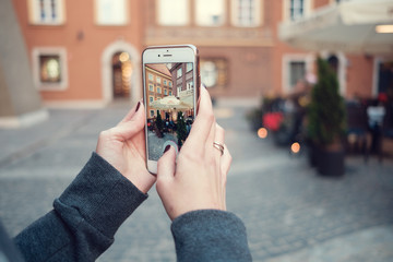 Back close up view of female person holding cellphone with and make photo. Woman's hands with mobile phone devise, finger touching display