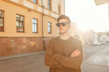 Wall Mural - Handsome fashion man model with a hairstyle with stylish sunglasses in fashionable clothes at sunset