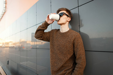 Wall Mural - Handsome fashionable man with hair in sunglasses with fashionable clothes drinks coffee