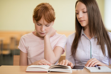 2 student girls are sitting at a desk