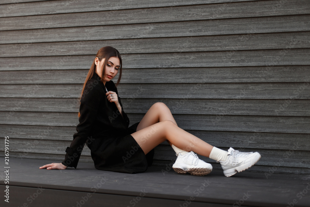 Beautiful fashionable sexy woman model in black coat and white sneakers ...