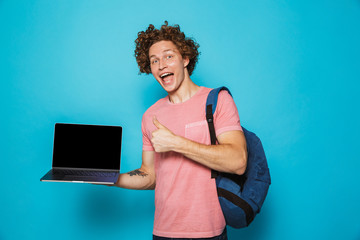 Poster - Photo of university guy with curly hair wearing casual clothing and backpack holding open laptop and showing thumb up, isolated over blue background