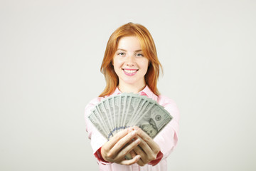 Portrait of young beautiful redhead woman with fistful of money holding one hundred dollar bill stack like fan. Excited attractive red hair female w/ lots of cash. Background, copy space, close up.