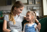 Fototapeta  - Smiling kid daughter looking at loving single mother hugging her on sofa, young woman mommy embracing cute happy girl showing care and support, sincere warm relationships of mom and child concept
