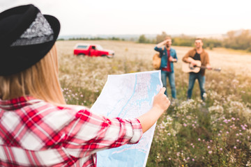 Wall Mural - close-up shot of woman looking at map during trip while her friends standing on background in flower field