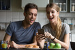 © fizkes - Excited young couple surprised by unbelievable good news, fantastic online travel offer looking at smartphone having breakfast together, happy family amazed by internet shopping sale in mobile app