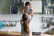 © fizkes - Rear view at happy mother holding excited kid daughter in the kitchen, single mom or sister playing lifting up cute girl laughing enjoying weekend together, family mum and child having fun concept
