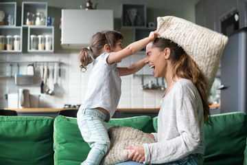 Mommy and kid daughter having pillow fight together, young babysitter nanny playing funny game with kid girl at home, happy mother and child enjoy spending time together, family leisure fun activity