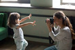 © fizkes - Mom photographer having fun playing making photo of artistic cute kid daughter at home, young mother photographing little child girl or shooting video on digital camera, funny family photo session