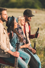 Wall Mural - group of young people drinking beer while sitting in car trunk in field