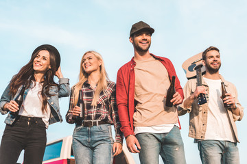 Wall Mural - bottom view of group of happy young people with beer bottles and guitar walking by field