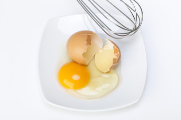 broken raw egg and wire mixing in a porcelain dish on a white