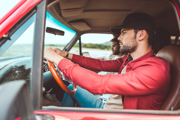 Wall Mural - side view of serious young men riding car in field