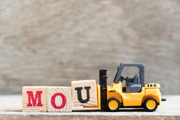 Wall Mural - Toy forklift hold letter block u in word mou (abbreviation of memorandum of understanding) on wood background