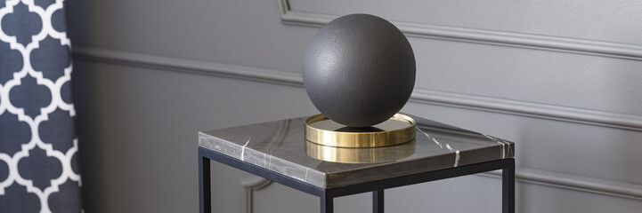 Real photo of a decorative boule standing on a table in living room interior with molding on a wall