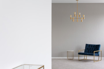 Gold chandelier above blue armchair in elegant living room interior in blurred background. Real photo with focus on an empty place on the wall for your product