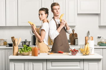 Wall Mural - young couple having fun and holding banana guns in kitchen