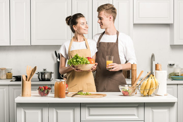 Wall Mural - young couple holding vegetables and glass of juice in kitchen