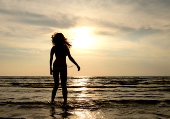 Wall Mural - Silhouette of a young woman in sea at sunset.