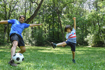 Wall Mural - Father and son play with ball in autumn park. Happy family play soccer in public park