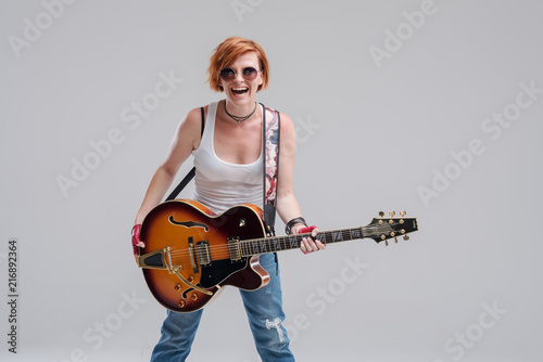 Cuadros en Lienzo Portrait of a young woman musician with an electric guitar in her hands on a gray background