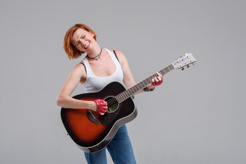 Wall Mural - Young woman musician with an acoustic   guitar in hand  on a gray background. He laughs and plays rock and roll loudly. 