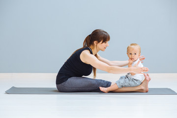 Wall Mural - Sportive brunette mother doing stretching, workout together on yoga mat over gray wall background. Athletic and healthy motherhood. Fitness, happy maternity yoga with children concept.