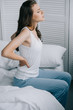 © LIGHTFIELD STUDIOS - side view of young woman in pajamas suffering from back pain on bed