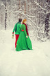 © irinashamanaeva - young couple, man and woman, husband and wife are walking in costumes of flowers typical of the elves of Santa's helpers in a winter forest under the snow with a chest full of gifts and a giant candy
