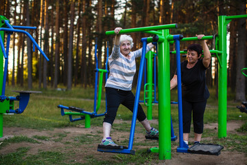 Wall Mural - An elderly woman with an adult daughter is doing exercises on the sport playground in the Park.