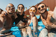 happy multiethnic friends in swimsuits and sunglasses posing in swimming pool