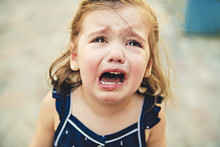 Close Up Portrait Of Crying Little Toddler Girl With Outdoors Background. Child