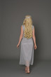 full length portrait of blonde girl wearing dress and crown. standing pose with back to the camera. grey studio background.