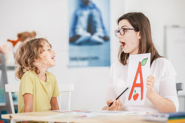 Wall Mural - Speech therapist working with a child on a correct pronunciation using a prop with a letter 'a' picture.