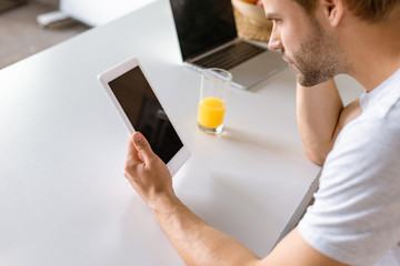 Wall Mural - man using digital tablet with blank screen at kitchen table with laptop and glass of juice