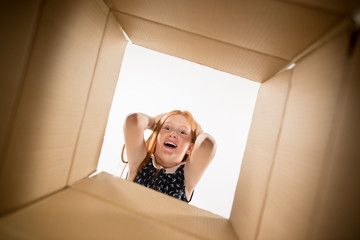 The surprised girl unpacking, opening carton box and looking inside. The package, delivery, surprise, gift lifestyle concept. Human emotions and facial expressions concepts