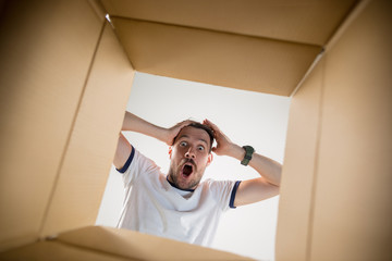 The surprised man unpacking, opening carton box and looking inside. The package, delivery, surprise, gift lifestyle concept. Human emotions and facial expressions concepts