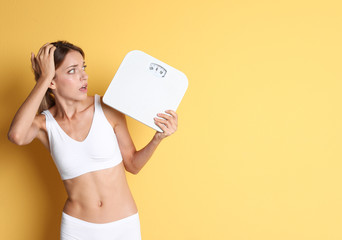 Wall Mural - Worried young woman holding bathroom scales on color background. Weight loss diet