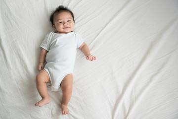 Adorable baby boy in white sunny bedroom in winter morning. Newborn child relaxing in bed. Family morning at home. Newborn kid during tummy time smiling happily at home