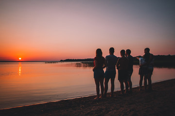 Silhouette of friends at the beach looking on the sunset in the summer evening