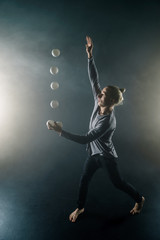 Wall Mural - Blond juggler with white balls on black background