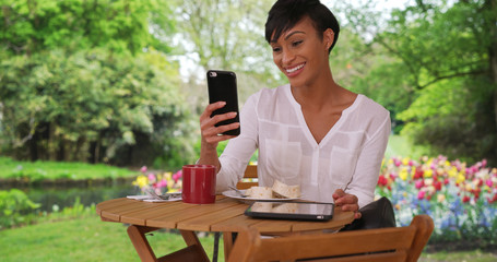 Mixed race female enjoying breakfast in garden facetimes friend via smartphone