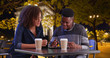 Smiling black male and female meeting for coffee at night use tablet